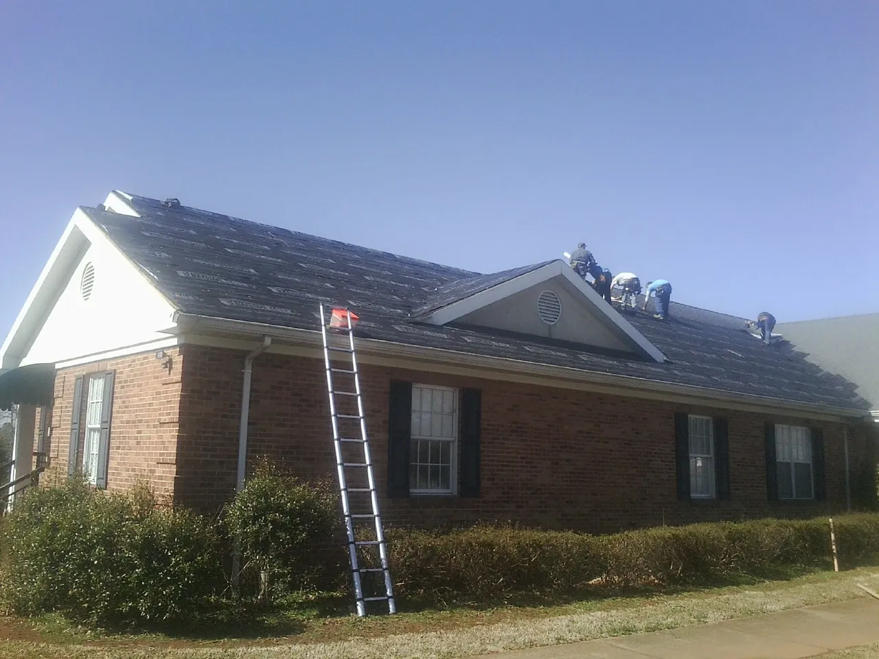 Crew tearing shingles off a brick ranch roof with a ladder set — Emergency Roof Repair work by our crew in Charlton