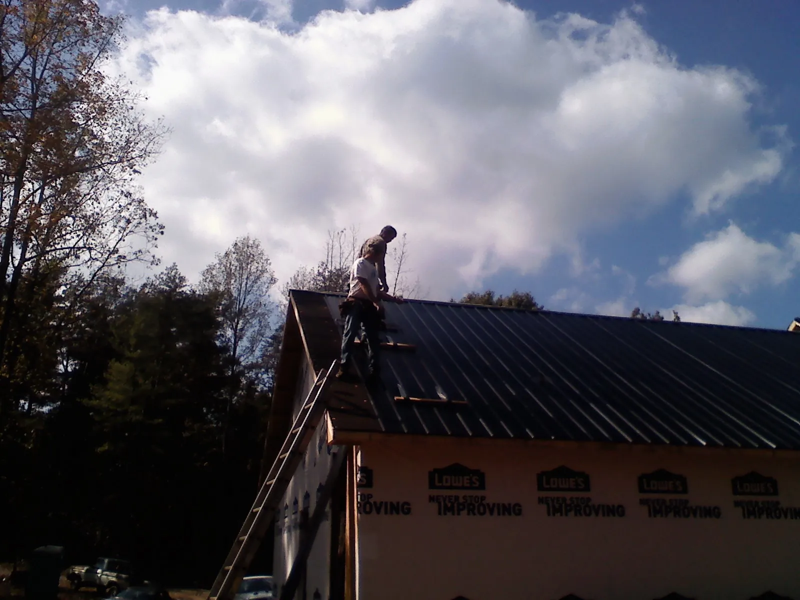 Roofer fastening dark metal panels high against a cloudy sky, from a Roof Inspection job in Charlton