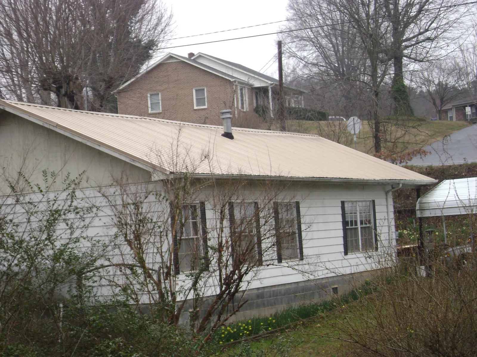 Tan metal roof on a white sided house set into a hillside — Commercial Roofing by Roofing Brothers in Charlton