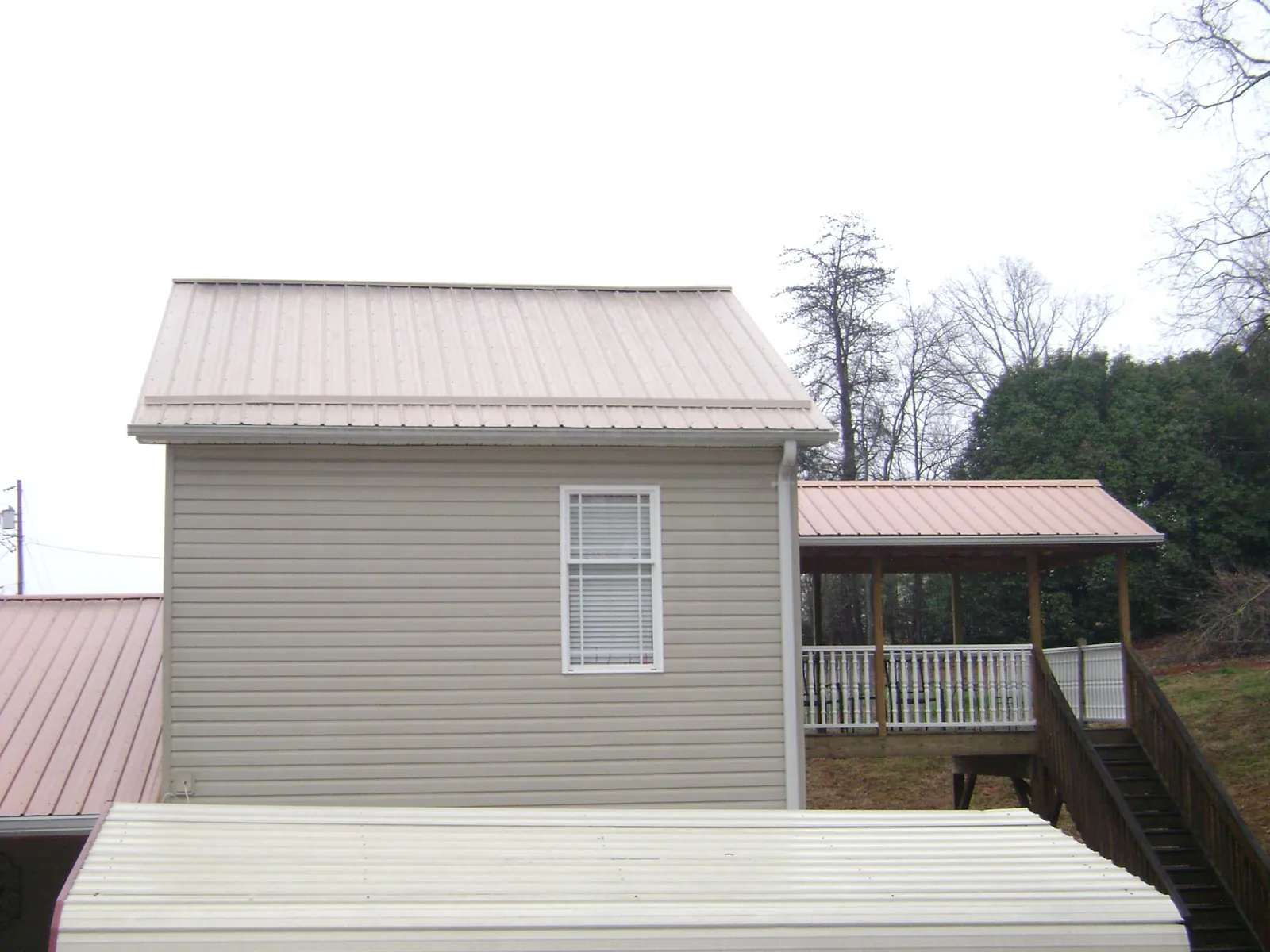 Tan metal roofs on a two story addition and attached porch, from a Roof Replacement job in Charlton